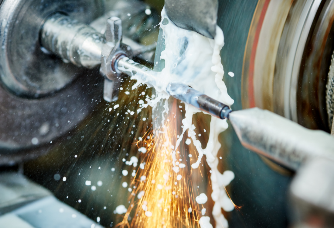 Close-up of a metal part being finished on a grinder machine, with sparks and coolant fluid spraying during the process, illustrating precision metal finishing.