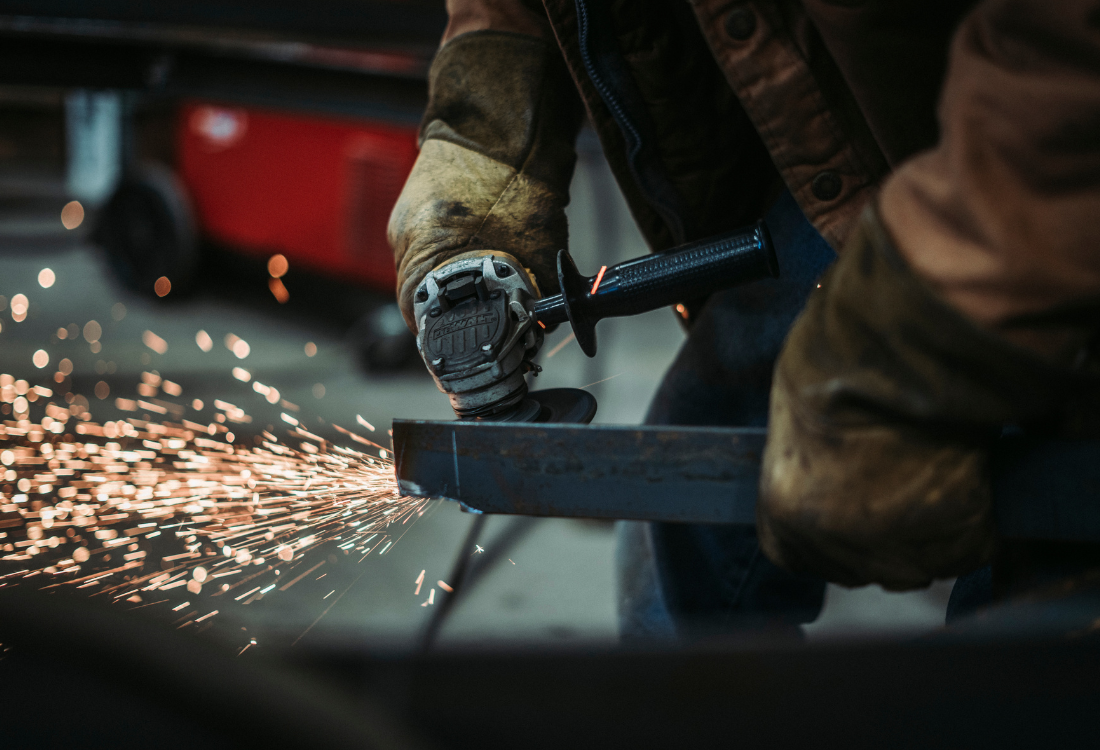  Worker manually grinding metal causing sparks, illustrating manual deburring and highlighting the importance of automated deburring machines in reducing HAVS risks.