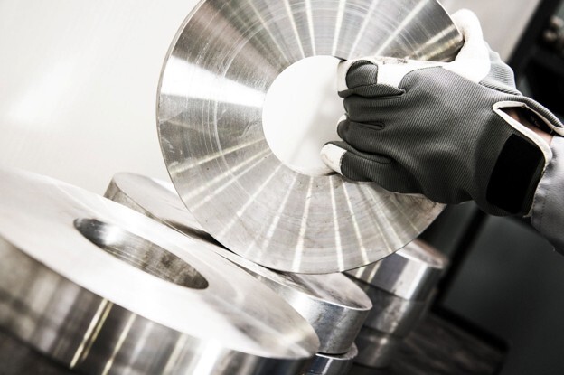Surface finishing machine used to process and smooth precision metal components, with a gloved operator handling polished metal discs. 